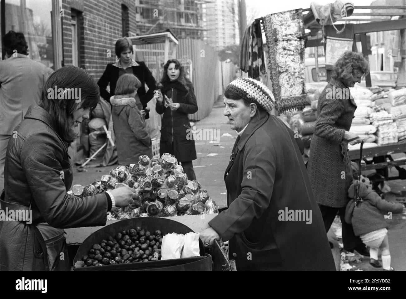 Castagne arrostite calde Londra 1970S. Commerciante di mercato in Roman Road, vende castagne arrostite calde e mele toffee con un esterno di toffee duro e fragile. Sono protetti da un involucro in cellophane trasparente per impieghi pesanti. Tower Hamlets, Londra, Inghilterra 1975 UK HOMER SYKES Foto Stock