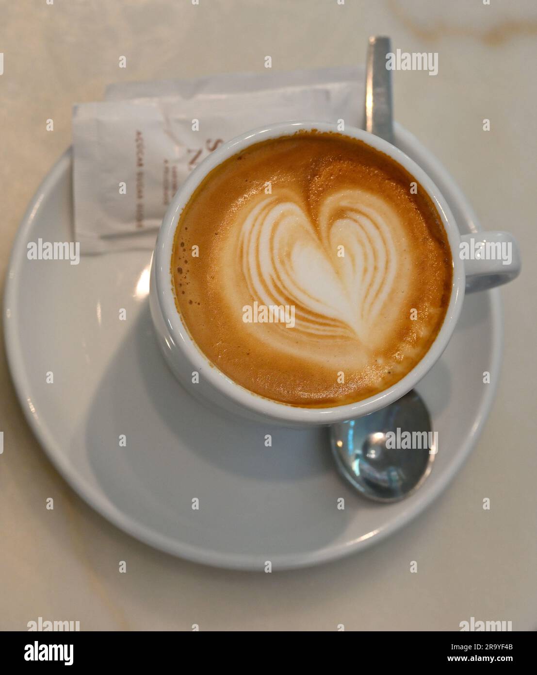 Tazza di caffè con schiuma di latte e cucchiaino sul piattino Foto Stock