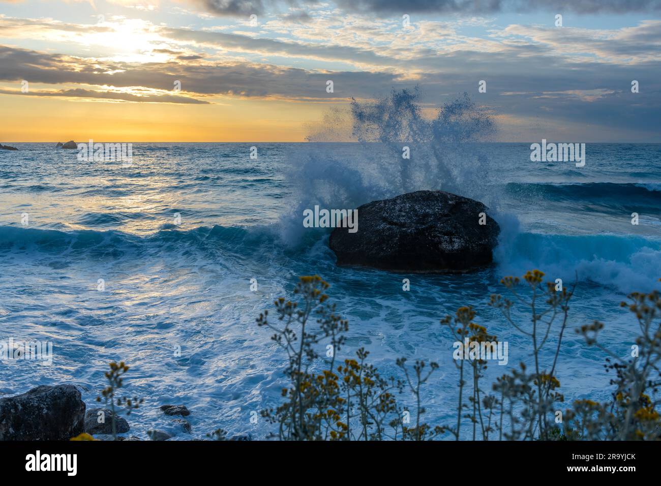 Un paesaggio marino di onde che si infrangono su una roccia durante il tramonto. Foto Stock