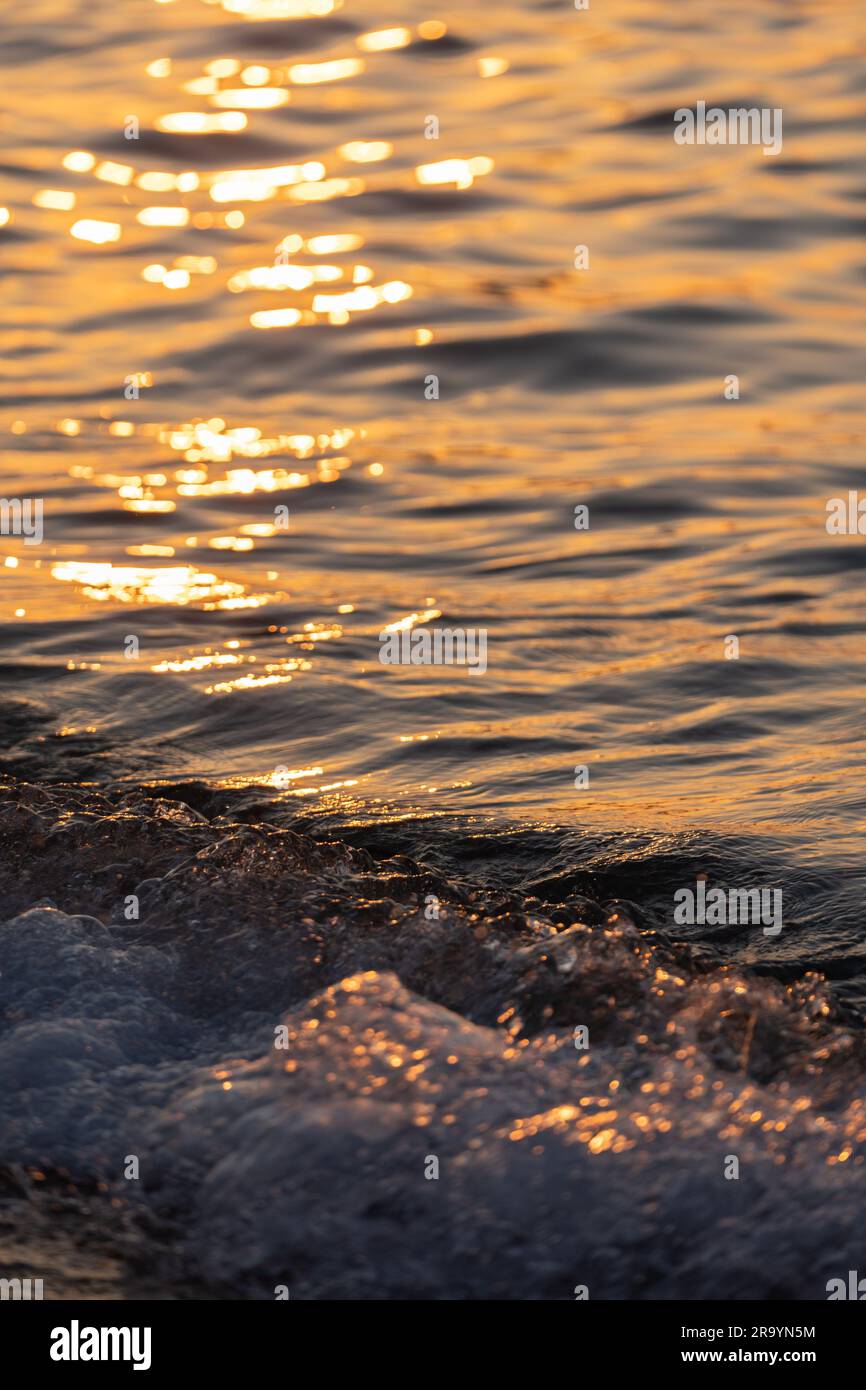 L'onda di mare spruzza da vicino. Ondulazione della superficie dell'acqua di mare con luce dorata del tramonto. Foto Stock