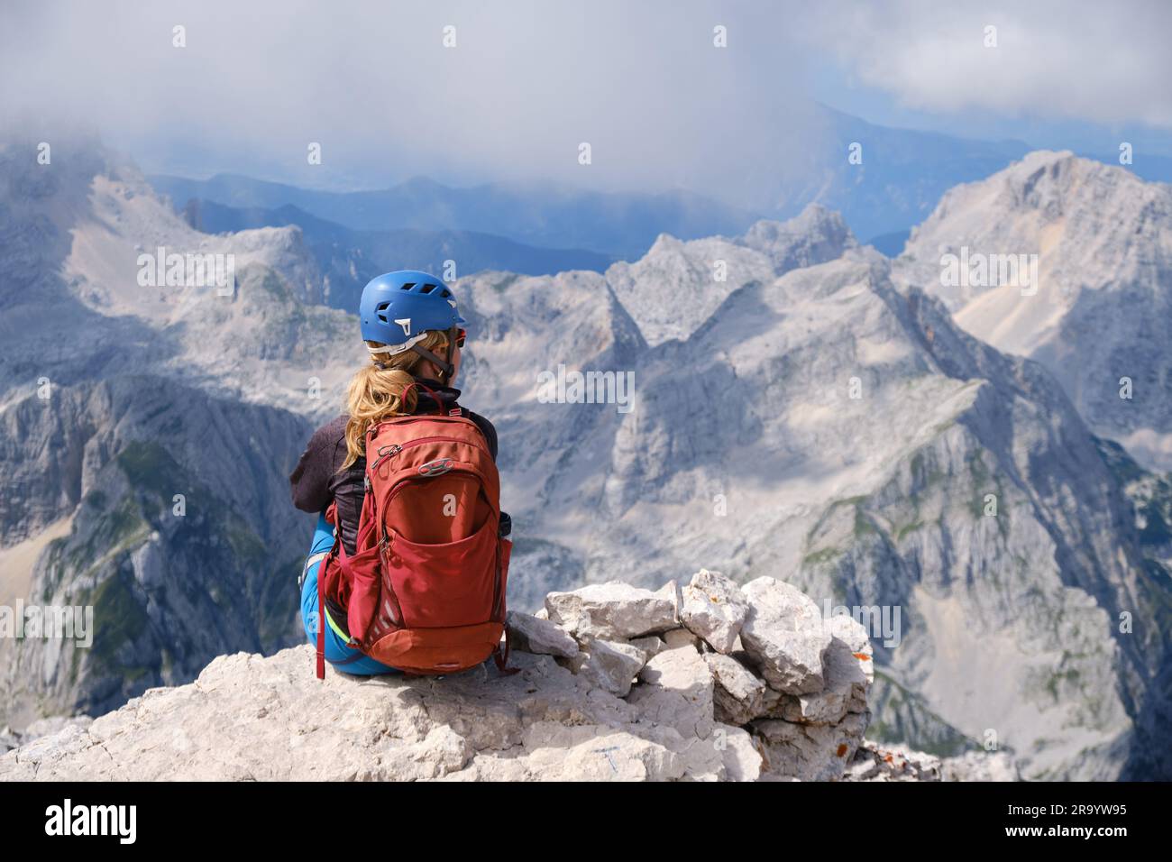 Donna alpina siede ai margini di una roccia nelle montagne del Triglav, in Slovenia, in una luminosa giornata estiva. Copia spazio, avventura, attivo, vertice, obiettivo, attività Foto Stock