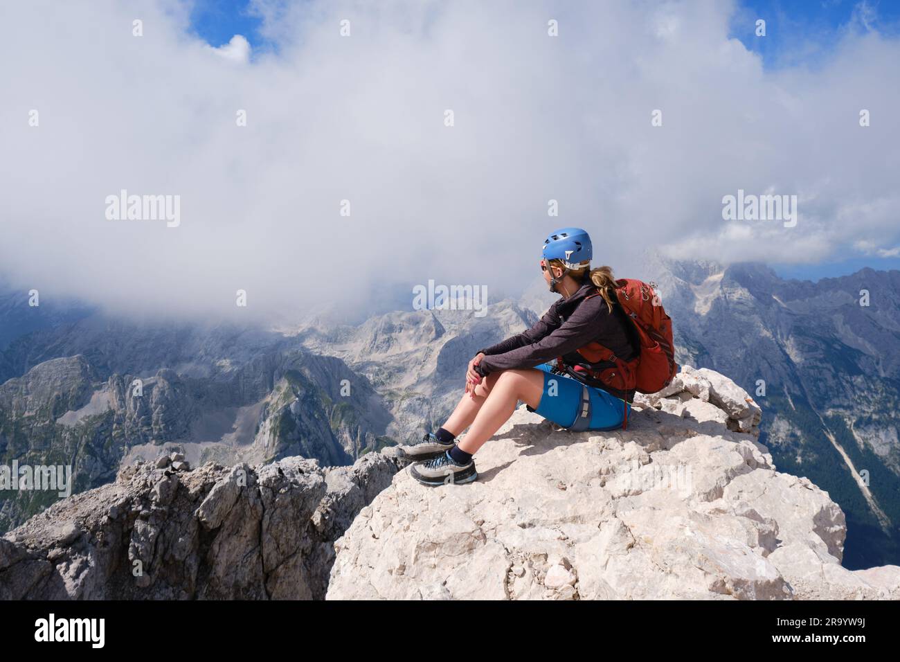 Una donna alpina siede su una roccia a Triglav Peak, in Slovenia, in una giornata estiva. Avventura, attiva, vetta, obiettivo, attività, montagna, parco nazionale, trekking. Foto Stock