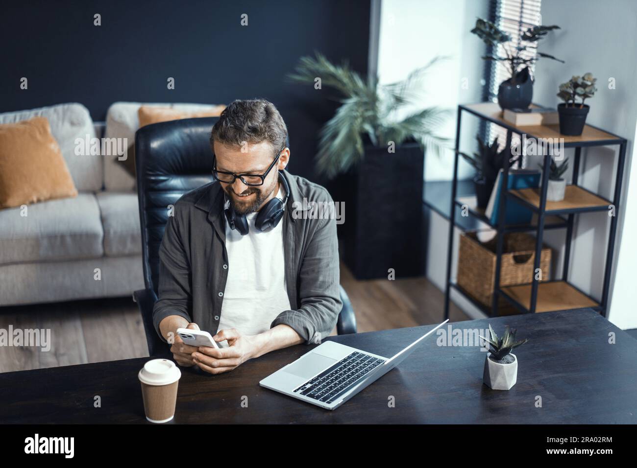 Concetto di lavoro da casa, con uomo di mezza età che lavora su un notebook. Uomo visto in un comodo ambiente di ufficio domestico, evidenziando la comodità e i vantaggi di lavorare comodamente dal proprio spazio. Foto di alta qualità Foto Stock