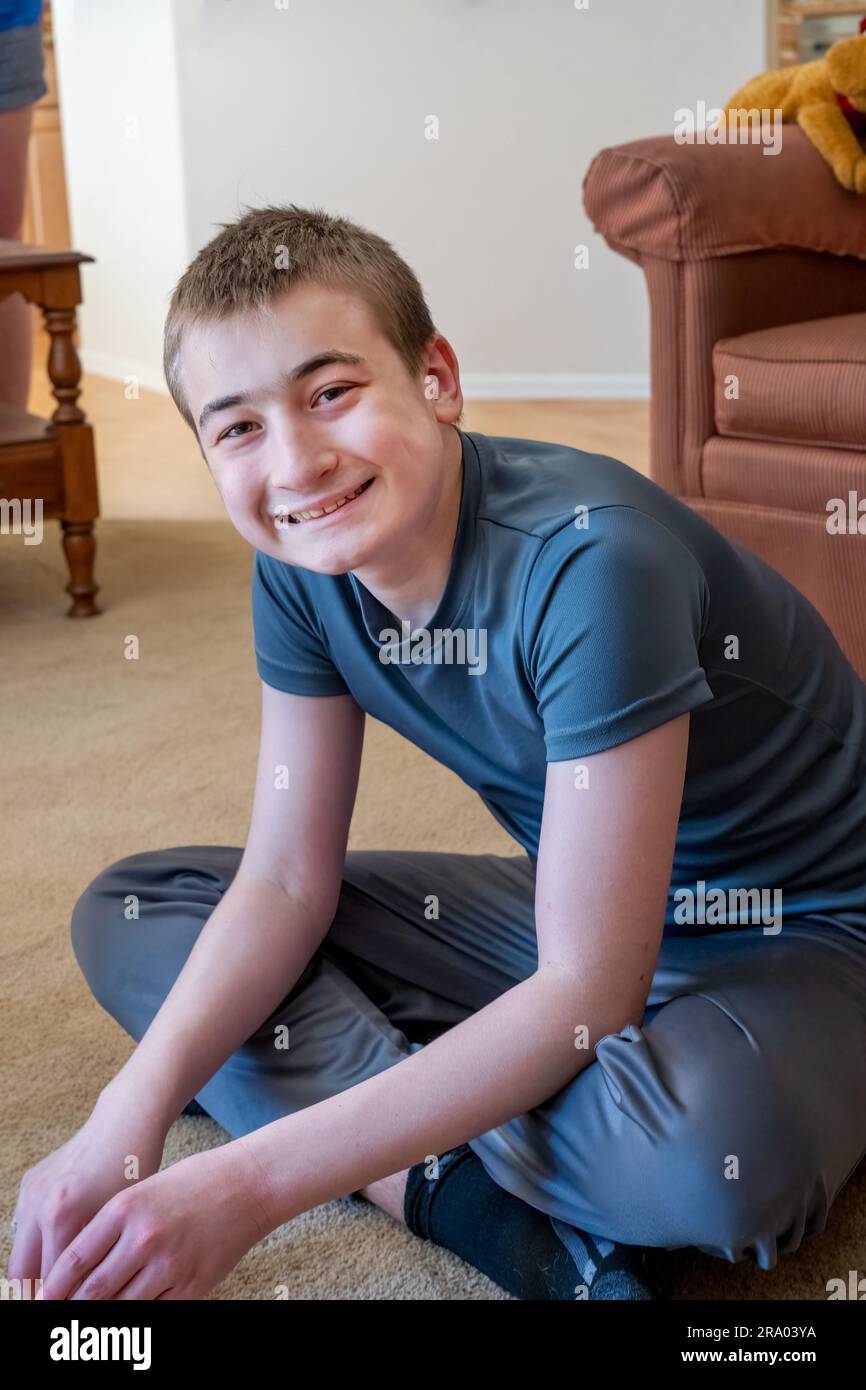 ragazzo di 15 anni seduto a gambe incrociate sul pavimento di un soggiorno sorridente. (MR) Foto Stock