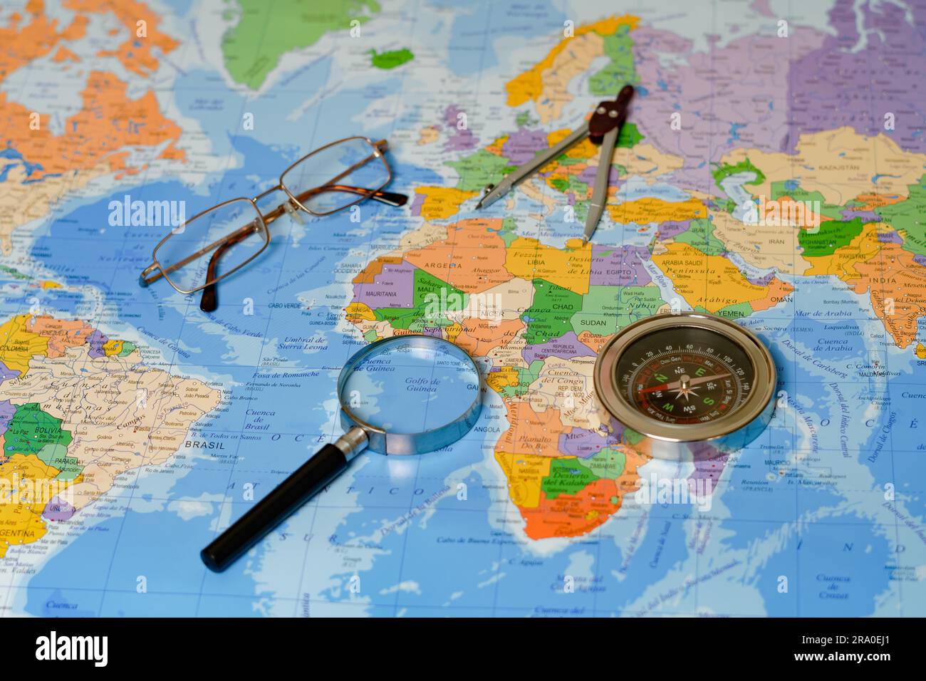 Su una mappa del mondo c'è una lente d'ingrandimento, una bussola, una bussola e degli occhiali Foto Stock