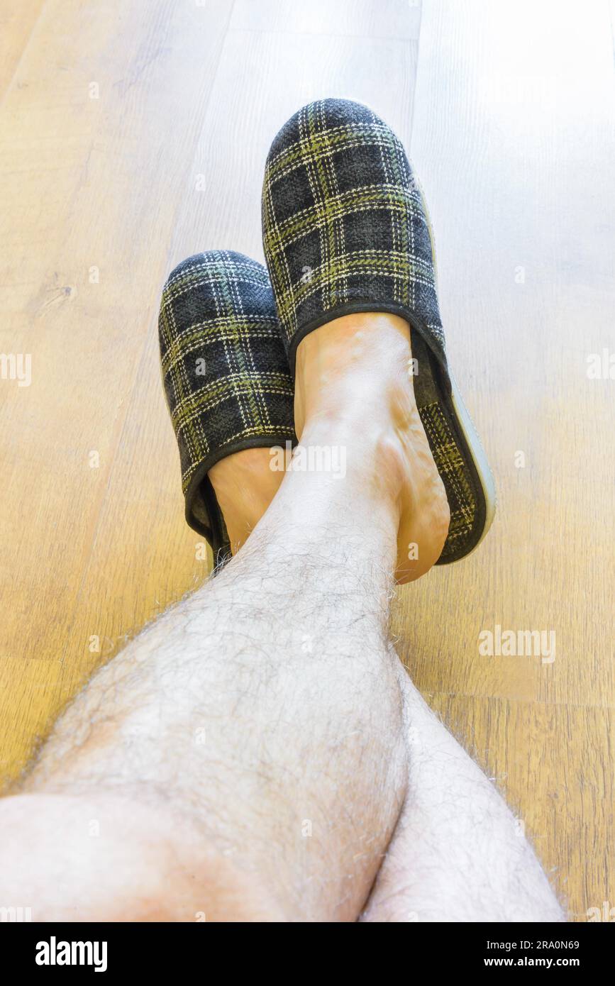 Un uomo è rilassante mentre indossa pantofole caldi e mostrando le gambe pelose Foto Stock