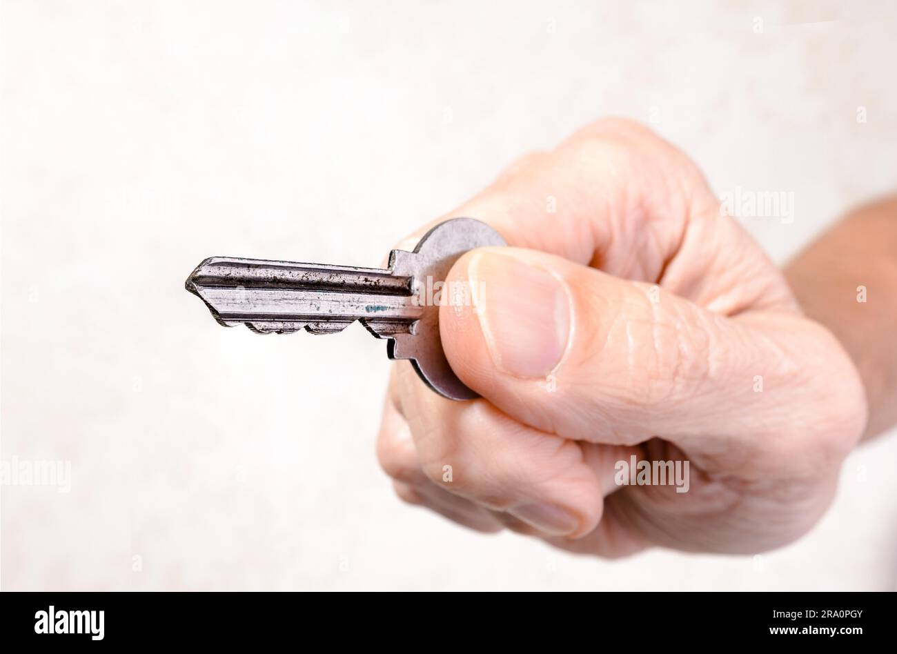 Una mano d'uomo è in possesso di una chiave di apertura o chiusura di una porta, su sfondo chiaro Foto Stock