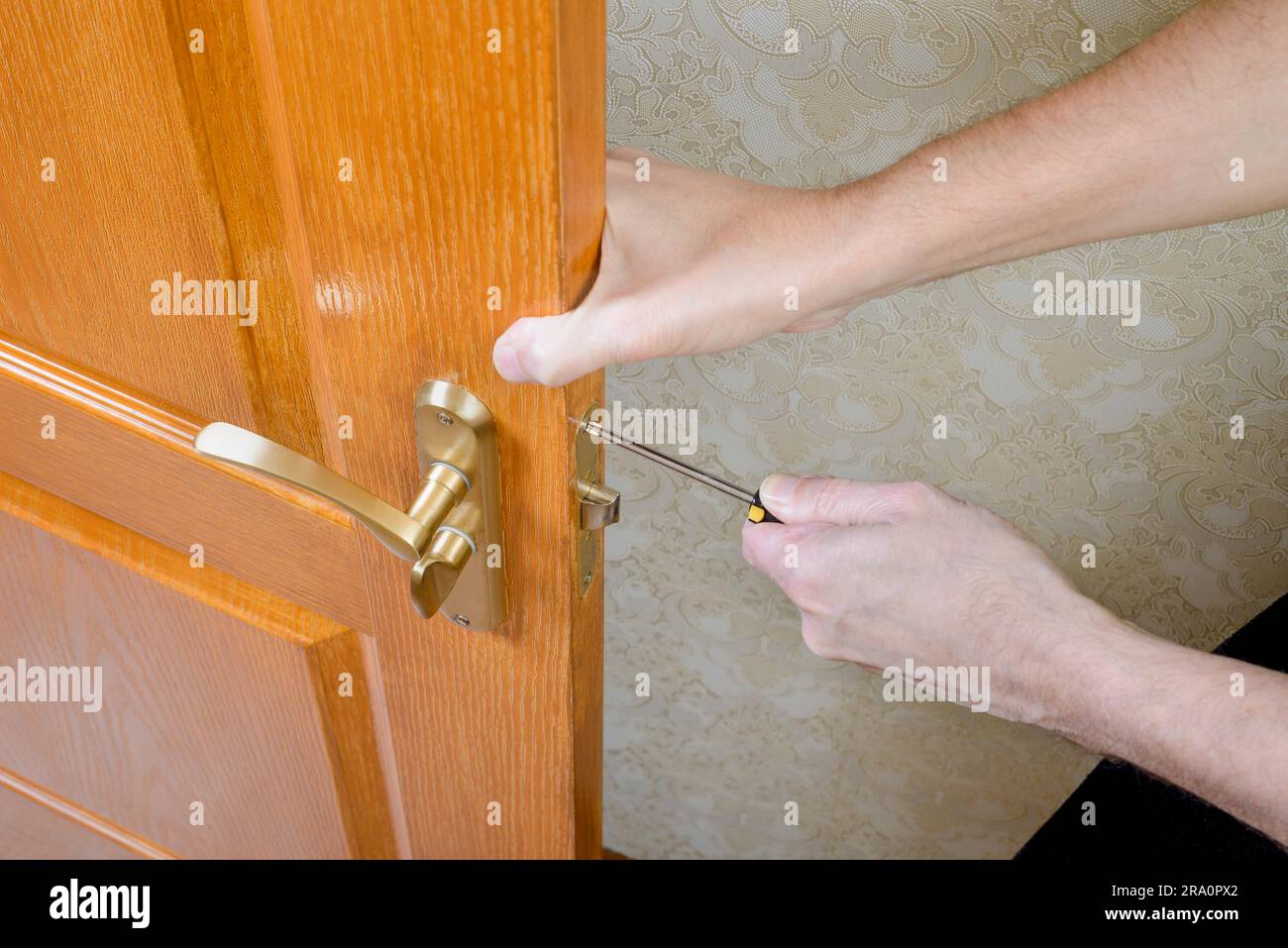 Un uomo è il montaggio della protezione sciopero del catenaccio su una porta con un classico stile curva maniglia in bronzo con un cacciavite Foto Stock