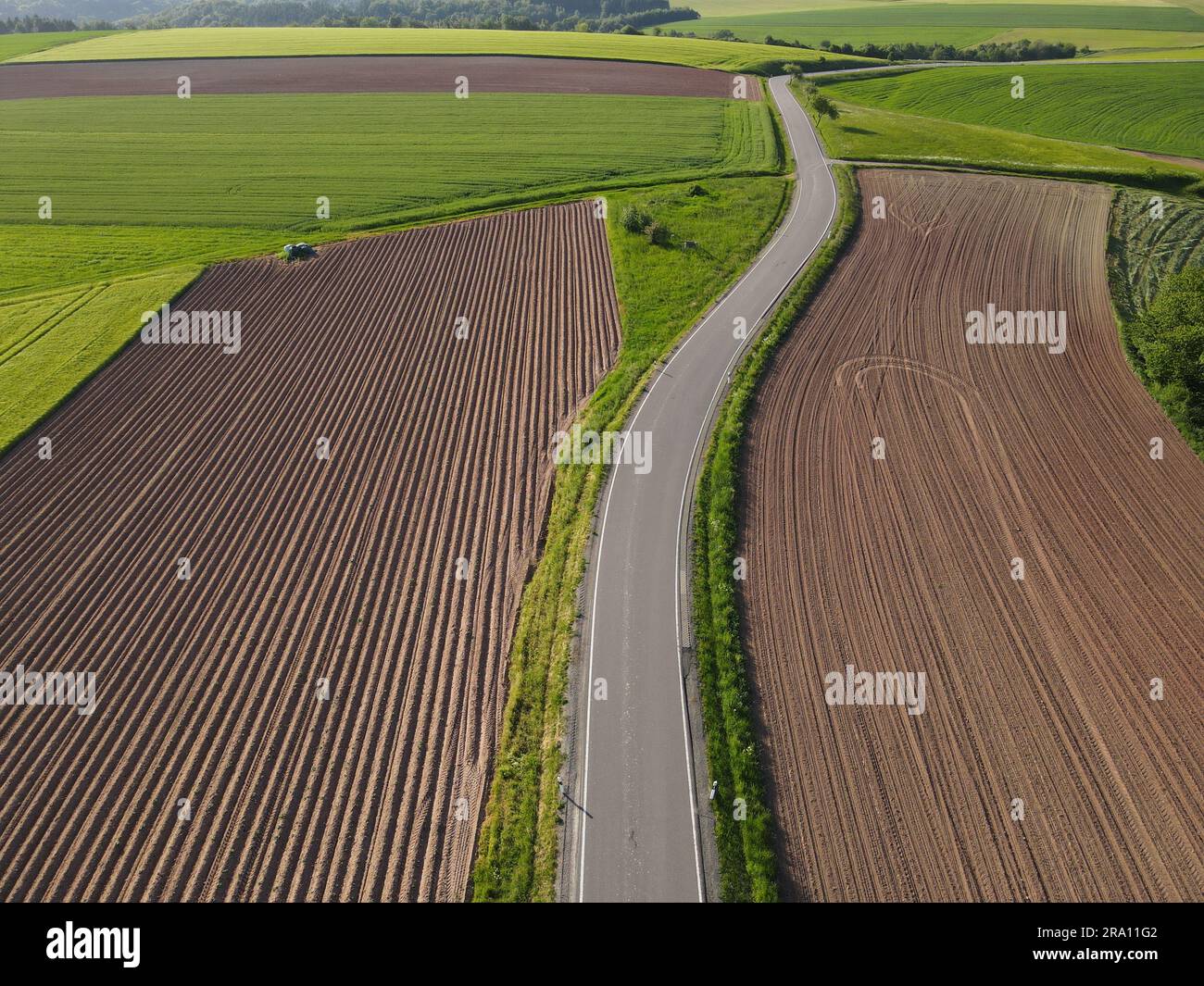 Lunga strada asfaltata tra terreni agricoli con terreno e grano dall'alto Foto Stock