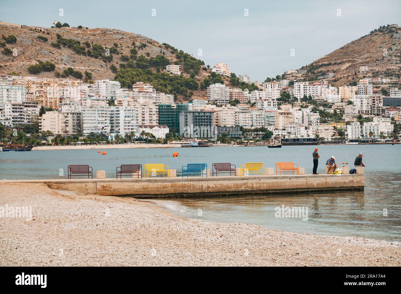 Un piccolo molo con colorate sedie in metallo sulla spiaggia principale di Sarandë, nella Riviera albanese Foto Stock