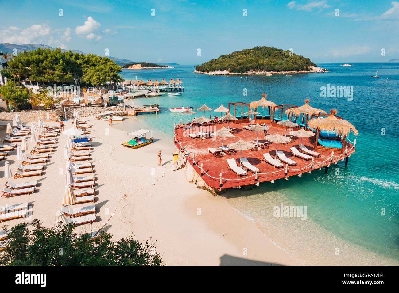 Lettini, ombrelloni, una terrazza in legno e acque turchesi che aspettano i turisti a Rilinda Beach, Ksamil, Albania Foto Stock