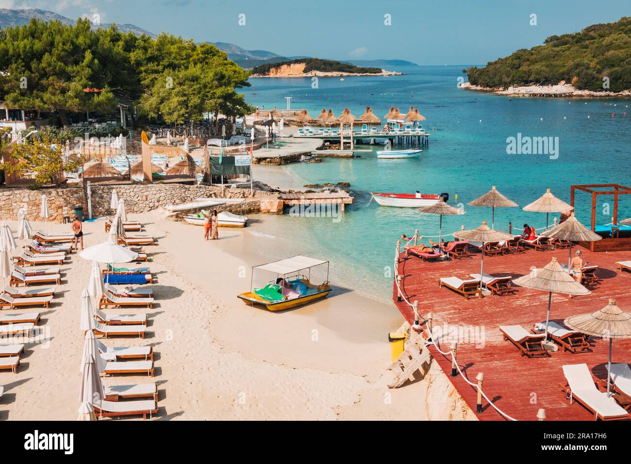Lettini, ombrelloni, una terrazza in legno e acque turchesi che aspettano i turisti a Rilinda Beach, Ksamil, Albania Foto Stock