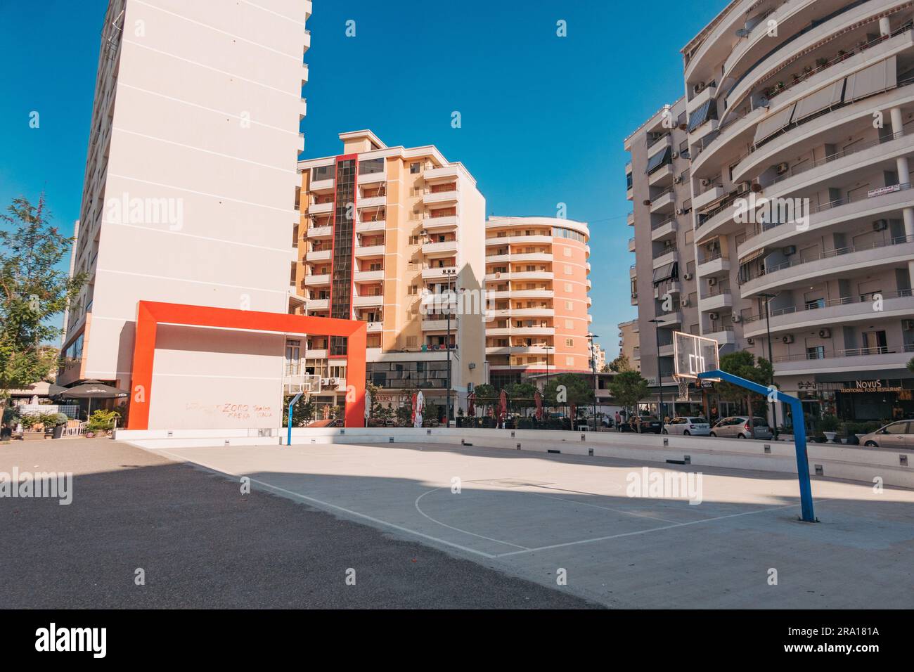 Un campo da pallacanestro pubblico tra blocchi di appartamenti con una grande scultura rettangolare rossa nella città costiera di Vlorë, nel sud dell'Albania Foto Stock