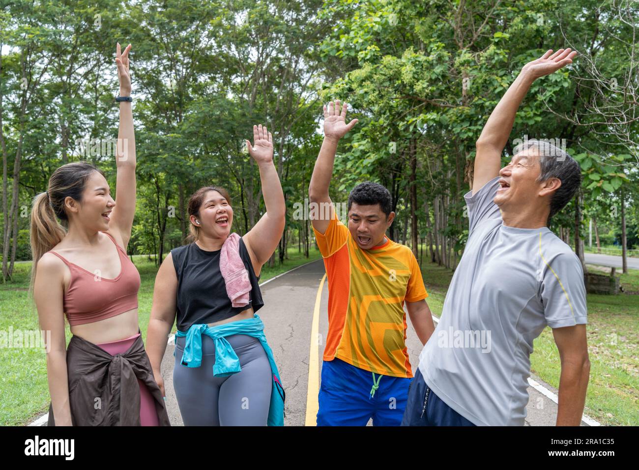 Un gruppo di 2 corridori maschi e 2 donne alzano le mani in aria per celebrare il loro successo in una pista di corsa di un parco locale Foto Stock
