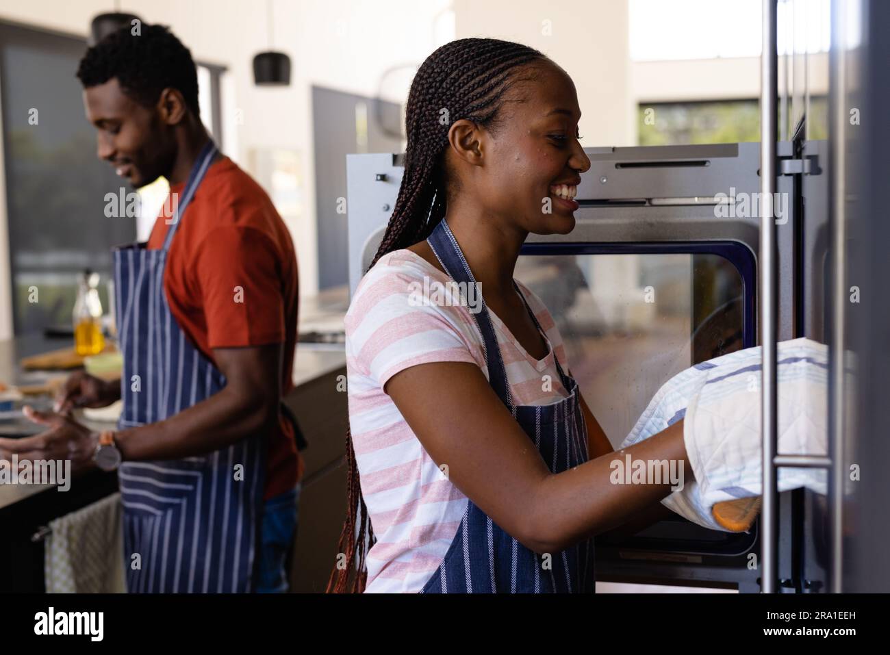 Felice donna afro-americana in grembiule che tira il pane cotto dal forno in cucina Foto Stock