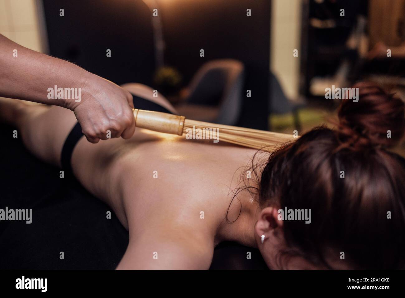 La massaggiatrice fa un massaggio alla schiena con bastoncini di bambù nel salone termale. Massaggio cervicale con scopa di bambù nel centro estetico o in clinica. La conc Foto Stock