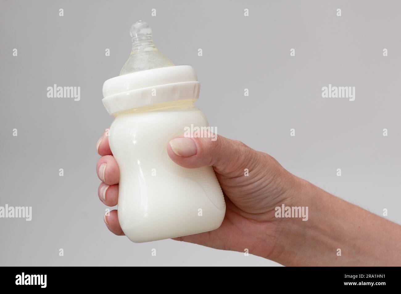 Allattamento al biberon isolato pieno di latte con mano di donna corta su sfondo bianco Foto Stock