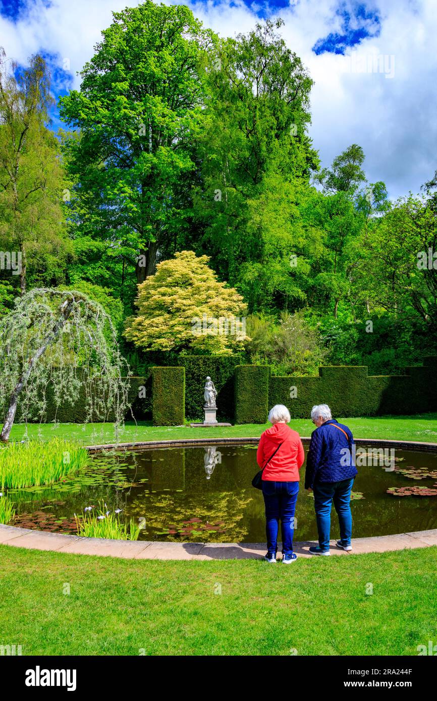 Due visitatori che si godono la tranquillità delle acque ferme nel giardino circolare della piscina presso il Knightshayes Court, nr Tiverton, Devon, Inghilterra, Regno Unito Foto Stock