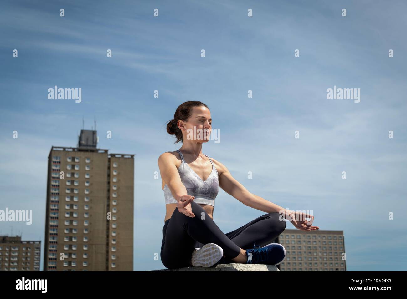Donna media adulta che pratica yoga e meditazione, sfondo urbano. Foto Stock