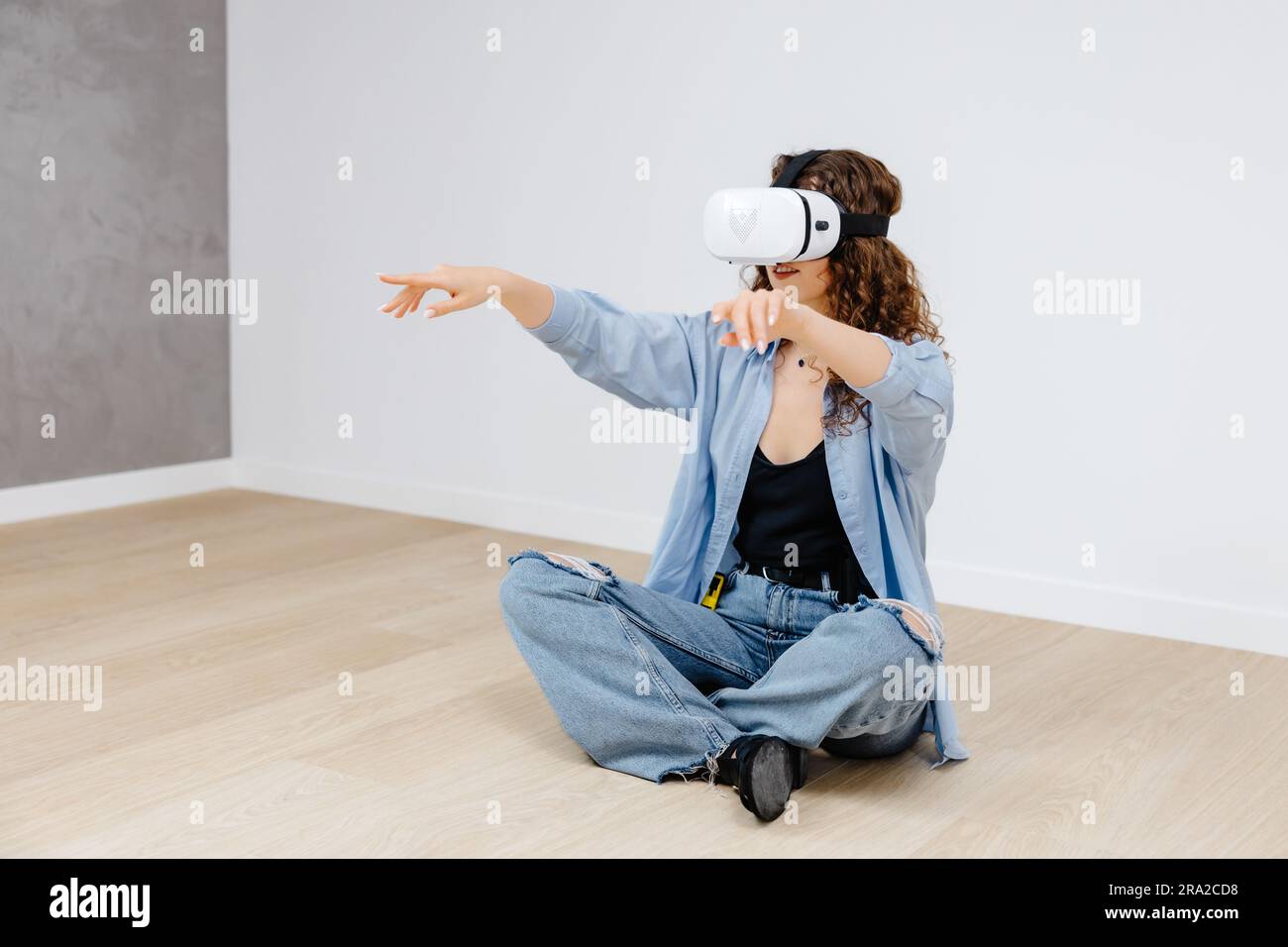 Giovane donna con occhiali per realtà virtuale che utilizza la tecnologia moderna per creare un design della stanza, muovere le mani in aria, stare in piedi in un nuovo appartamento durante la ristrutturazione. Reale virtuale Foto Stock