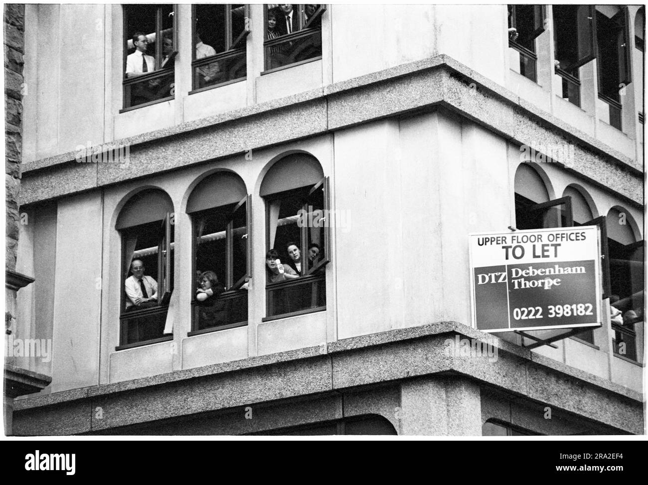 I lavoratori in ufficio guardano dalle finestre mentre i Bon Jovi giocano un concerto gratuito sul palco di Queen Street, Cardiff, Galles, Regno Unito il 21 giugno 1995. Il concerto era quello di pubblicizzare il concerto poco venduto all'Arms Park Stadium il giorno successivo. Foto: Rob Watkins Foto Stock