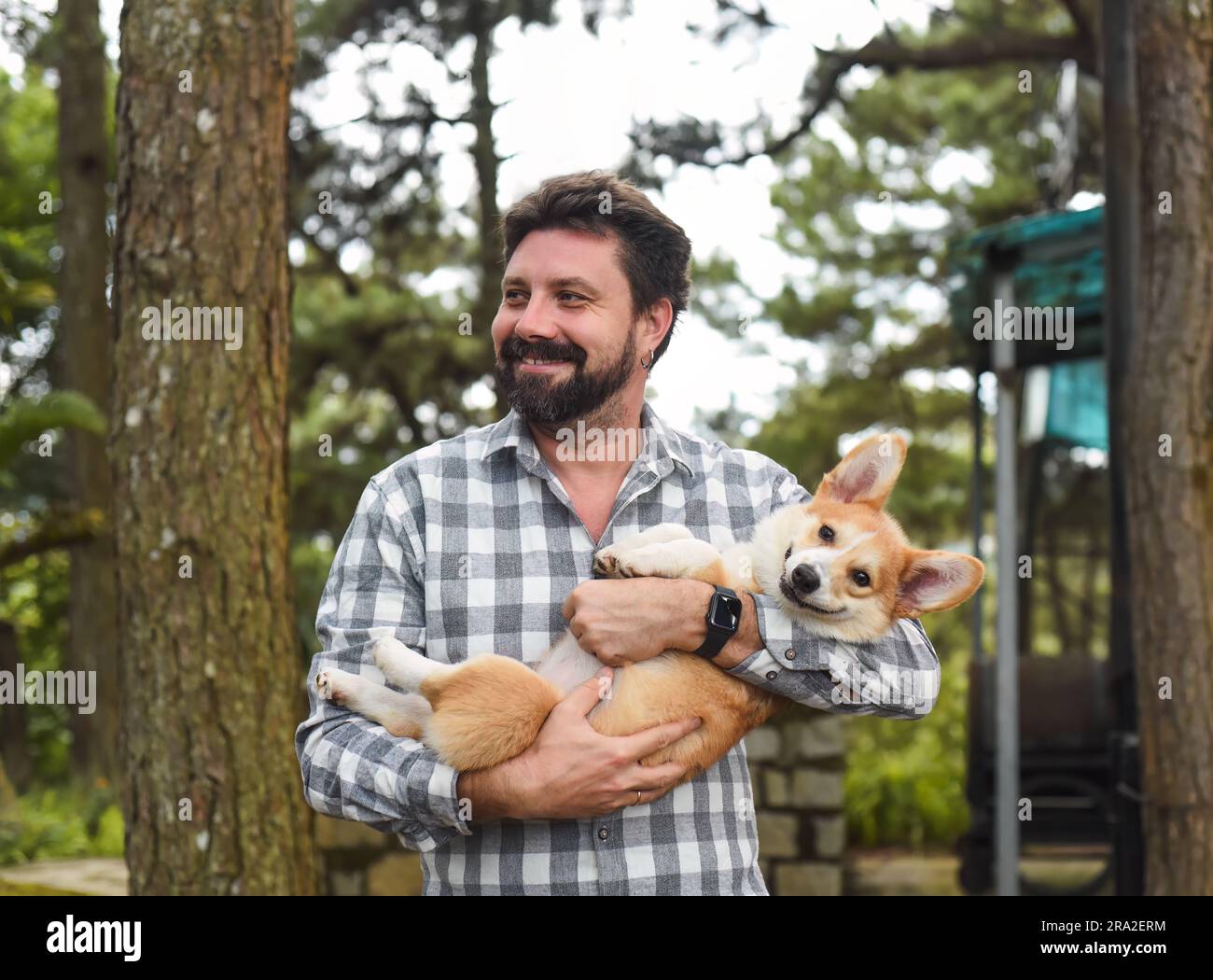 Un uomo dalla barba felice che tiene in mano il suo cane corgi gallese e sorride Foto Stock