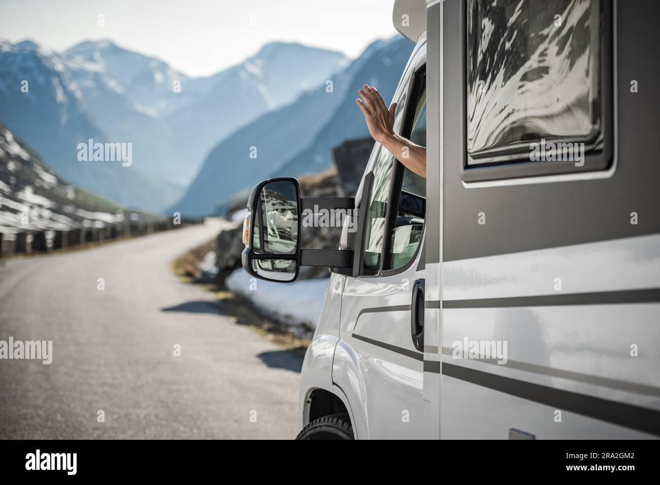 Autista di camper caucasico con gesti amichevoli mentre si viaggia attraverso il paesaggio panoramico. Tema Van Life. Foto Stock