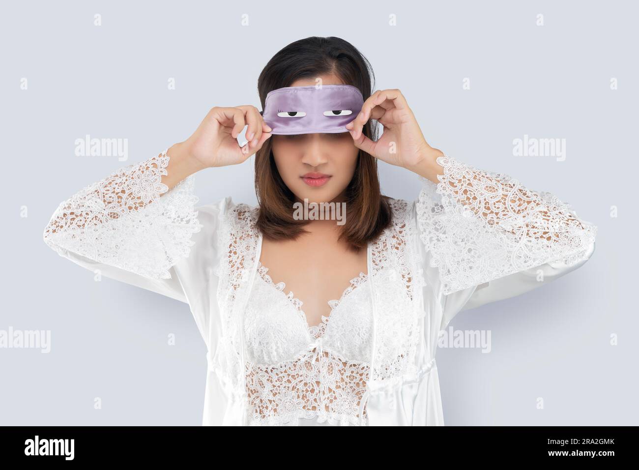 Donna asiatica in abito da notte in pizzo e abito in raso bianco togliere una maschera per il sonno o una maschera per gli occhi dopo il risveglio al mattino Foto Stock