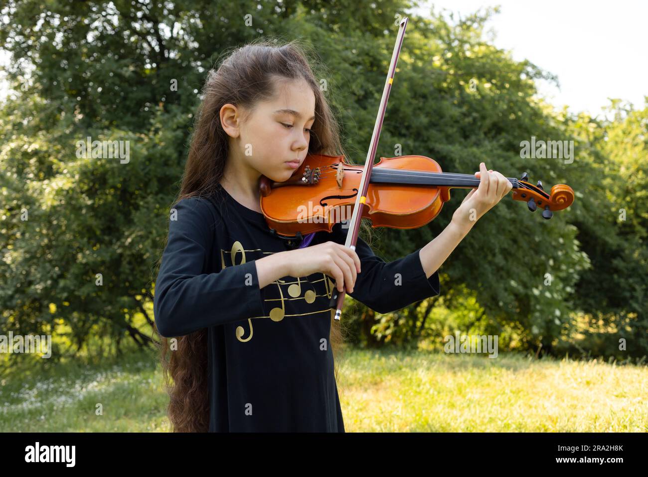 Asiatica caucasica - bambino suona su violino, strumento musicale a corda, Green Park sullo sfondo. Little Adorable Child, artista di talento, stile di vita Foto Stock