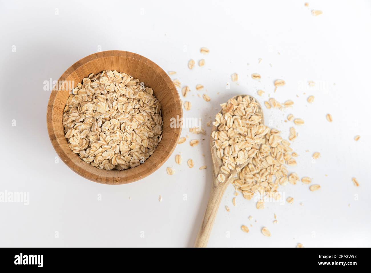 Cucchiaio di legno pieno di fiocchi d'avena prelevati da una ciotola di legno su sfondo bianco. Alimenti super ricchi di sostanze nutritive che possono essere utilizzati per diverse ricette. Foto Stock