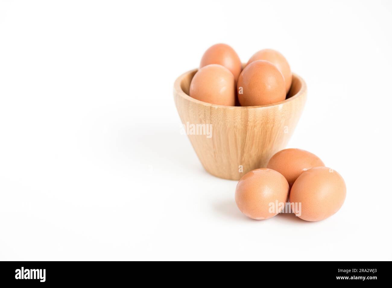 Diverse uova di gallina fresche poste dentro e fuori un contenitore di bambù su sfondo bianco. Copia spazio. Foto Stock