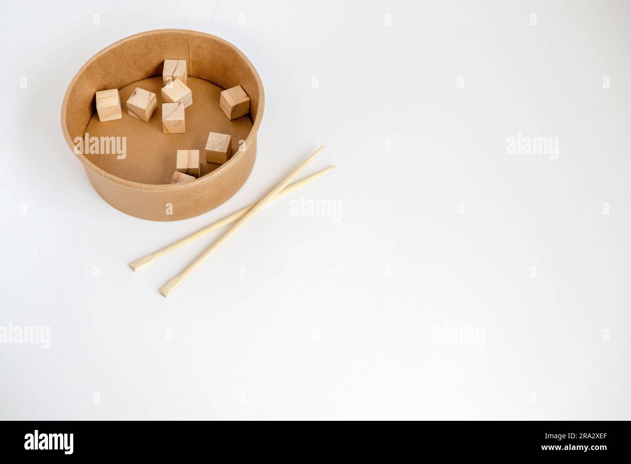 Bacchette di bambù e scatola di carta riciclata con cubi di legno all'interno su sfondo bianco. Immagine concettuale Foto Stock