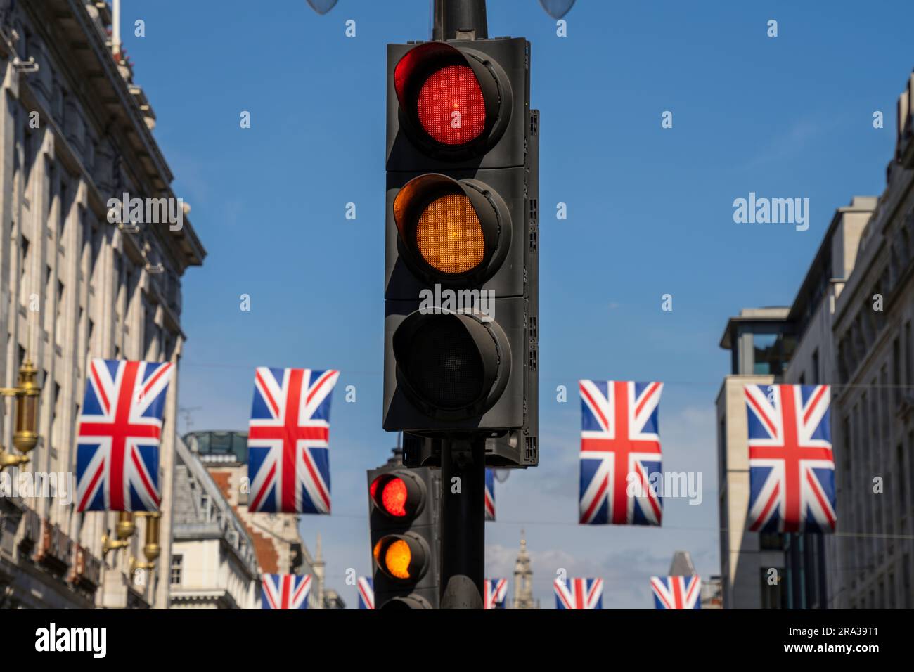 Semaforo giallo e rosso su una strada cittadina di Londra con bandiere inglesi. Segnali contrastanti e confusi, metafora concettuale per scelte di vita. Foto Stock