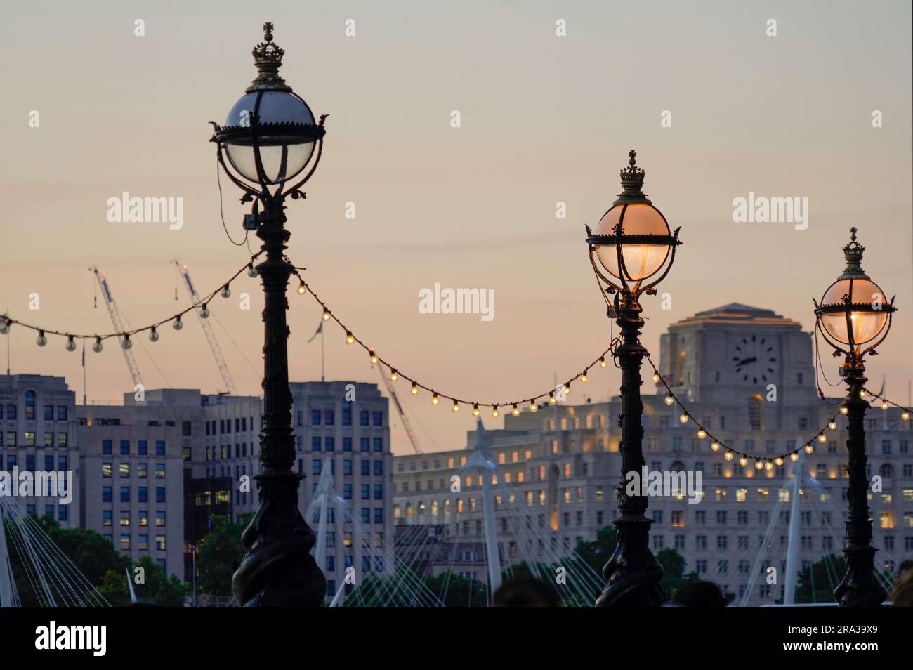 Passeggiata sul Tamigi a Londra al crepuscolo con lampioni decorativi. Alcuni dei lampioni sono accesi mentre altri sono spenti. Un semaforo rotto. Foto Stock