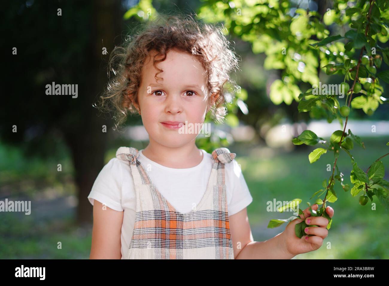 Ritratto di una bambina carina con i capelli ricci che rimane in giardino, sfondo naturale Foto Stock