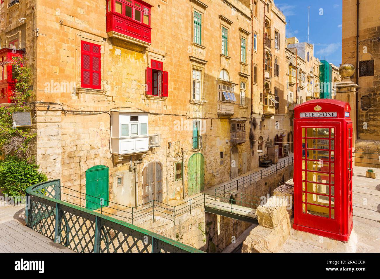 La Valletta, Malta - la tradizionale strada maltese con cabina telefonica rossa, persiane e balconi e cielo blu in una giornata di sole nella capitale di Malta Foto Stock