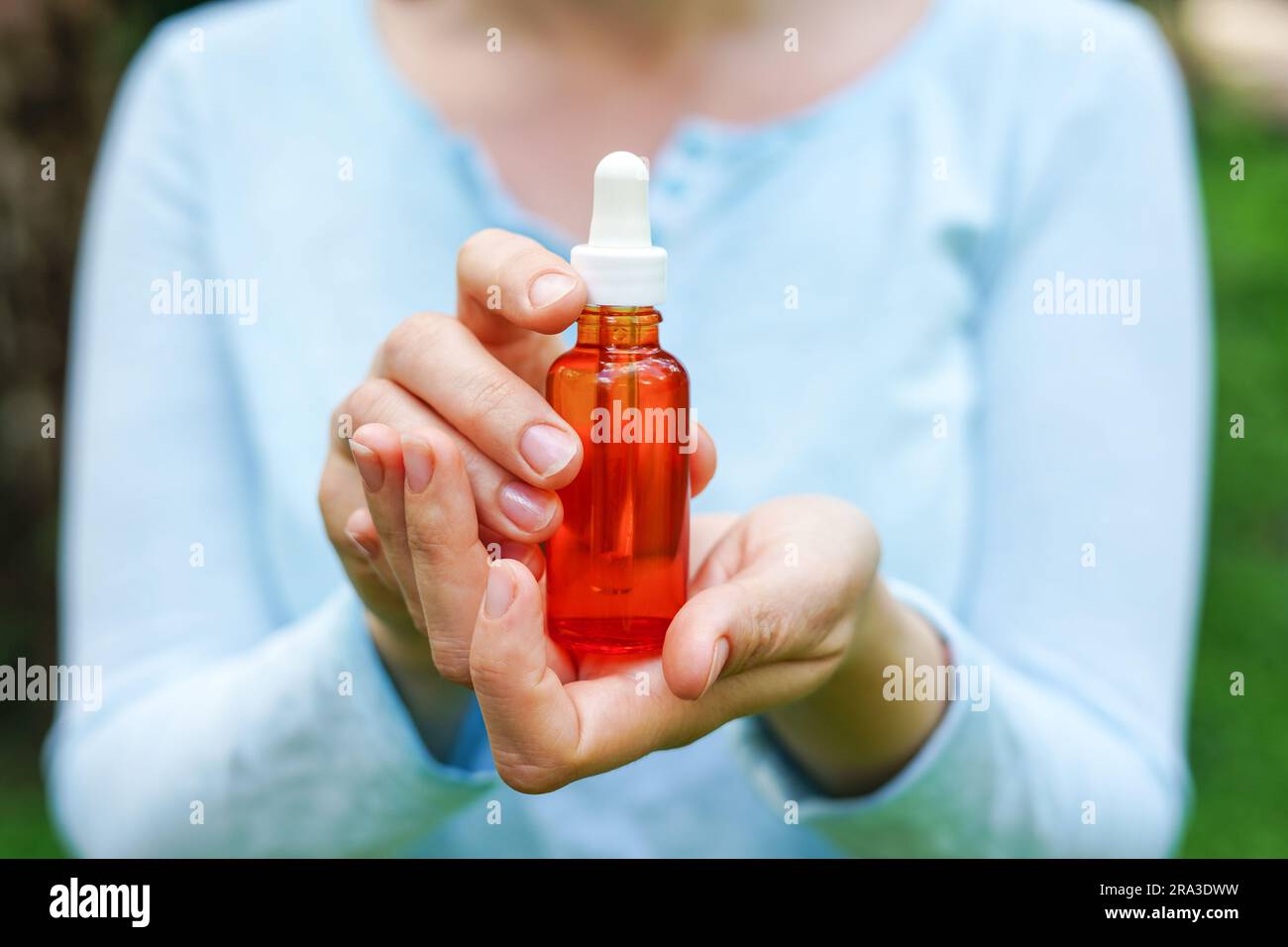 Donna in tessuto blu con bottiglia di vetro rosso con olio cosmetico spa. saloni terapeutici, prodotti naturali per la cura del corpo Foto Stock