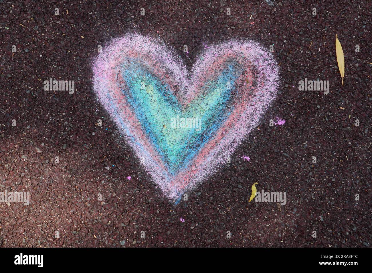 Segno del cuore disegnato con gesso di colori pastello sul pavimento in gomma del parco giochi Foto Stock