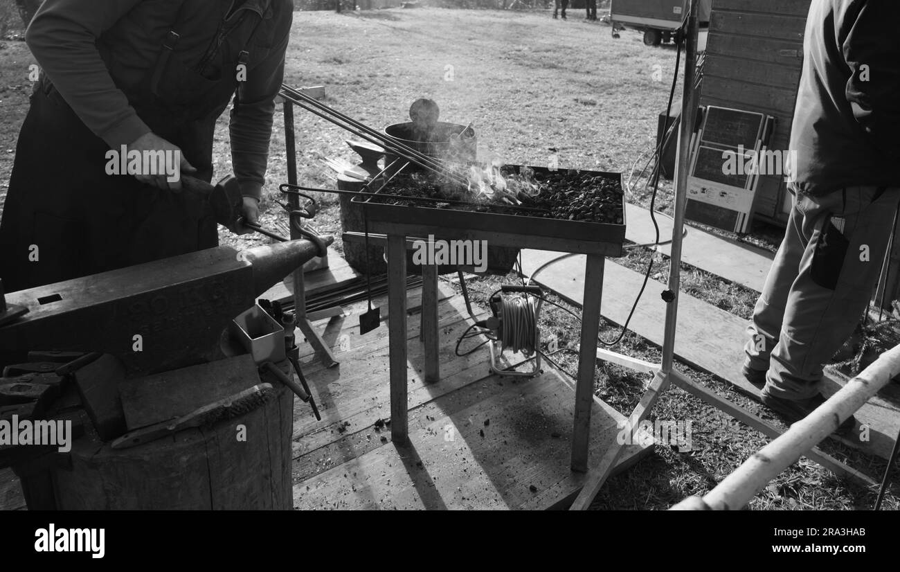 Fabbro con ferro rosso-caldo e fuoco a carbone aperto al lavoro Foto Stock