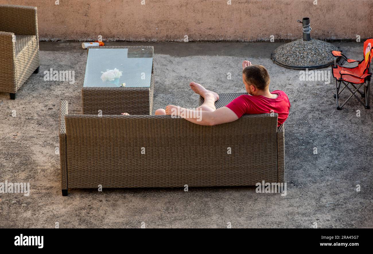 uomo che si rilassa in un giardino seduto su un divano arredato in rattan. Foto Stock