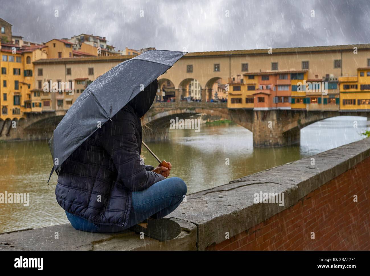 Ragazza sotto ombrellone al lungofiume Arno nel centro di Firenze in un giorno di pioggia, in Italia Foto Stock