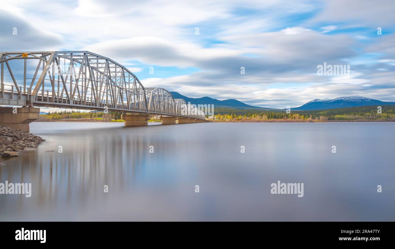Grande ponte in acciaio costruito dall'uomo che attraversa la baia di Nisutlin nella cittadina di Teslin che scorre verso il fiume Yukon nel Canada settentrionale durante la primavera Foto Stock