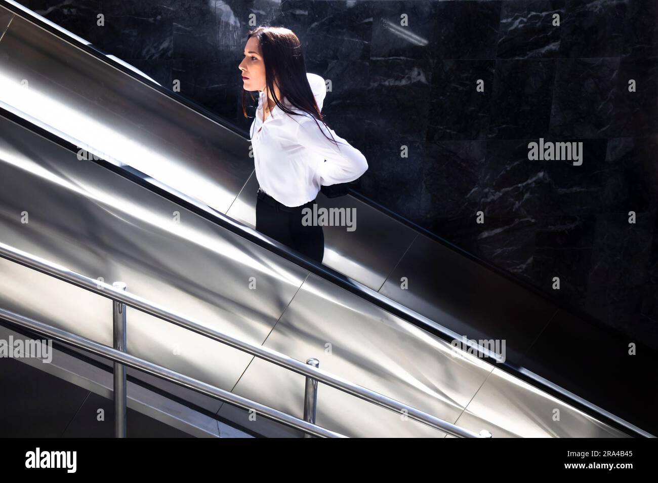Belgrado, Serbia - 15 giugno 2022: Giovane donna con camicia bianca e pantaloni neri che sale sulla scala mobile della metropolitana, in una giornata di sole Foto Stock