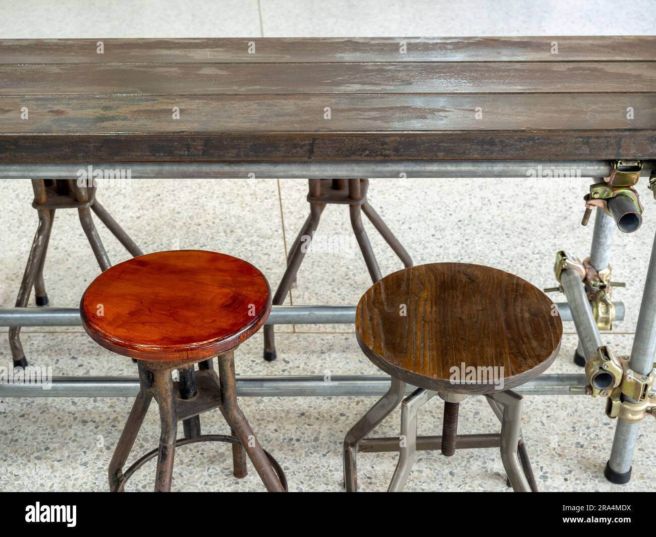 Due sedie rotonde d'epoca vuote sotto un tavolo in legno decorate su fondo pavimento in cemento, interni di un edificio in stile loft. Sedia girevole in legno, metà secolo f Foto Stock