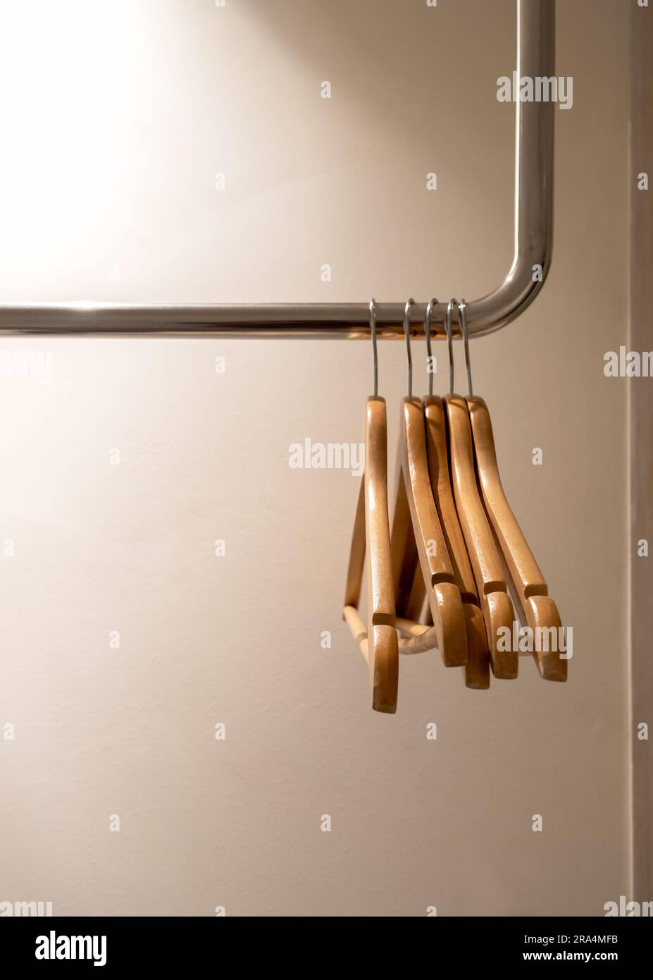 Cinque appendiabiti vuoti in legno senza camicie o abiti appesi a una guida d'acciaio nel guardaroba su sfondo bianco con spazio per le copie, preparandosi per il Foto Stock