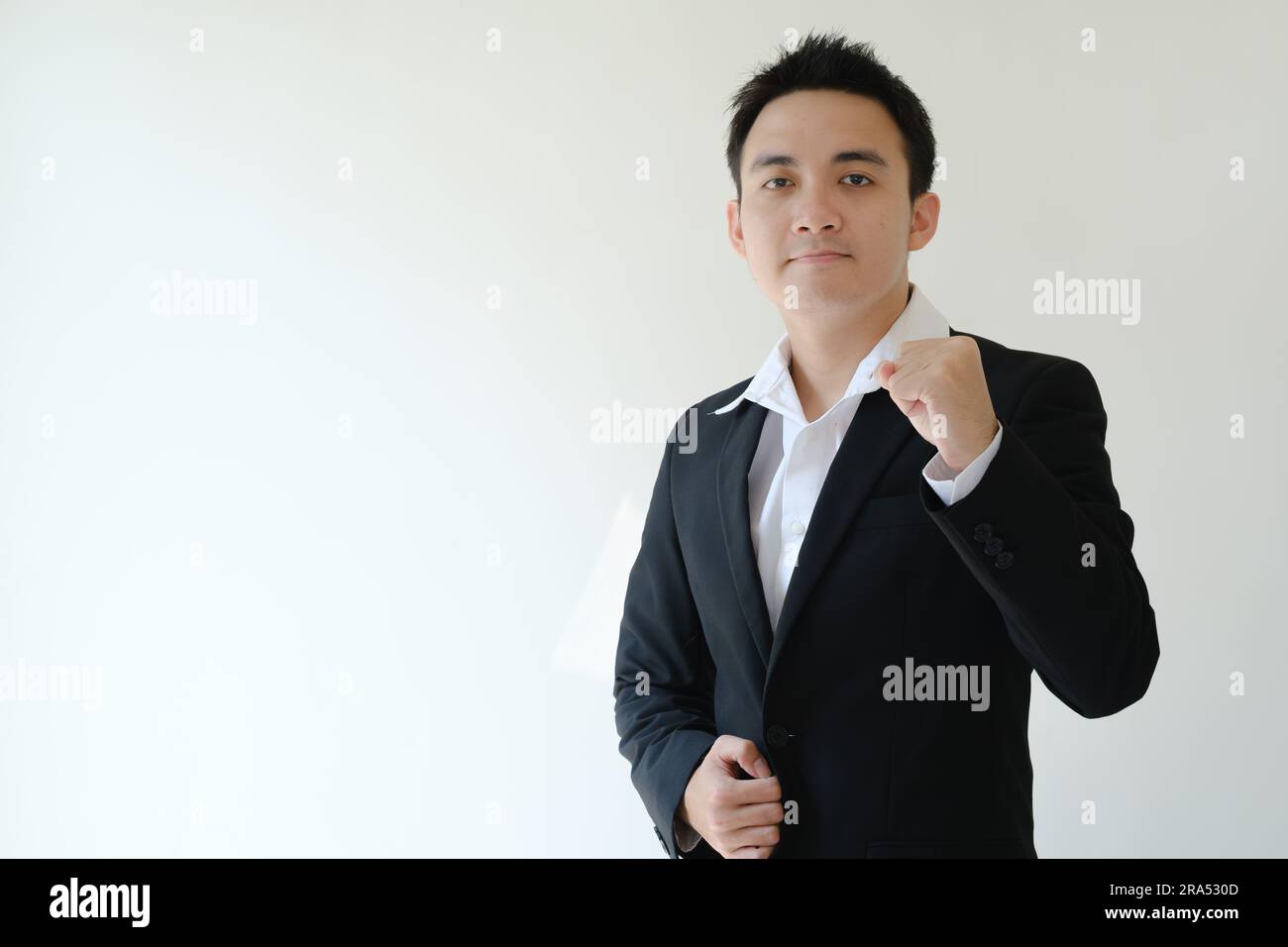 Giovane uomo d'affari asiatico con espressione del volto piatto che stringe il pugno e guarda la fotocamera. Sfondo bianco isolato. Foto Stock