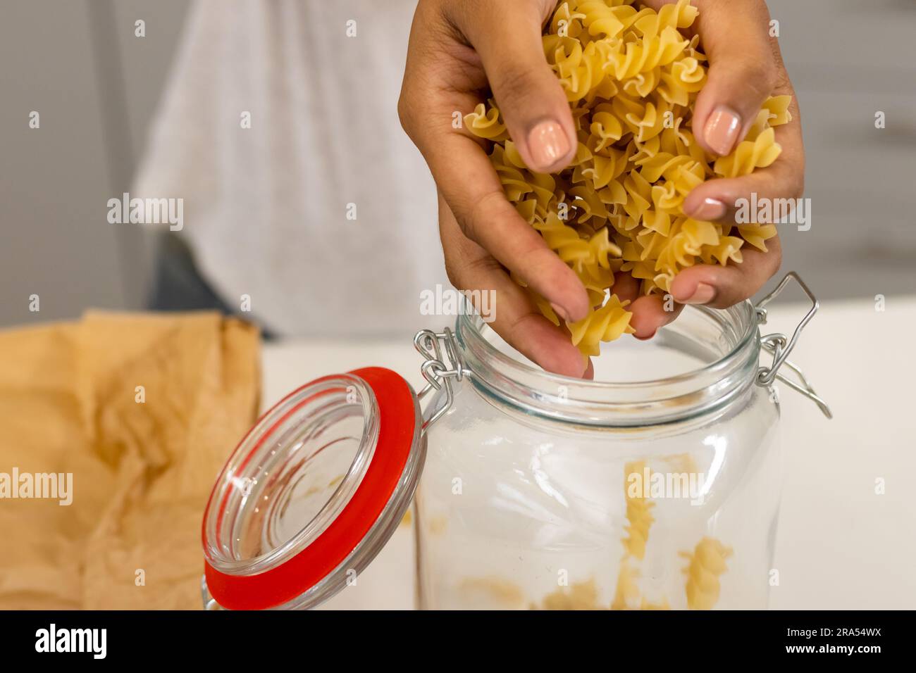 Mani di donna birazziale che versano nel vaso di conservazione in cucina Foto Stock