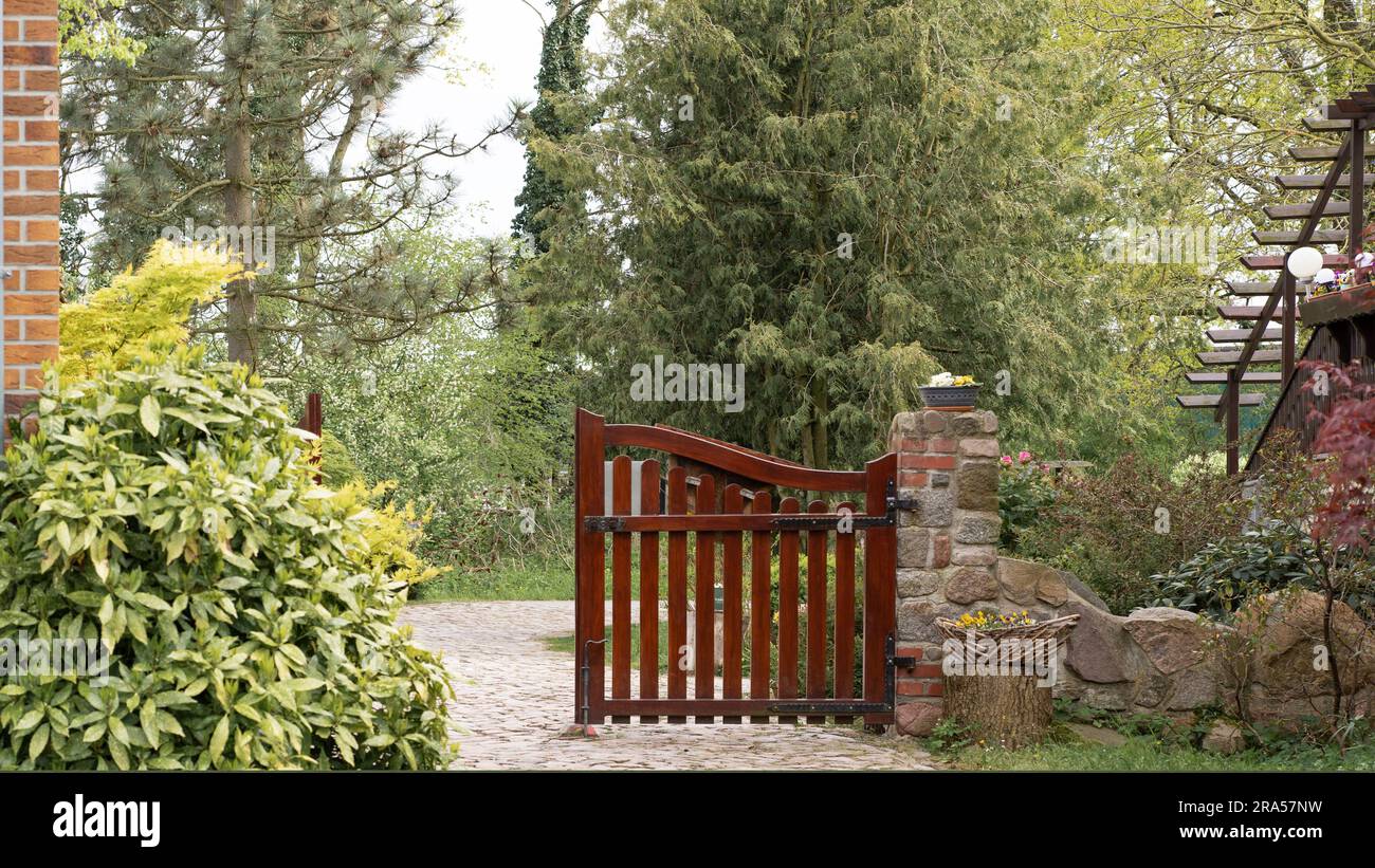 Bellissimi cancelli in legno marrone in un giardino verde, una parte leggermente aperta, che vi invitano all'interno. Foto Stock