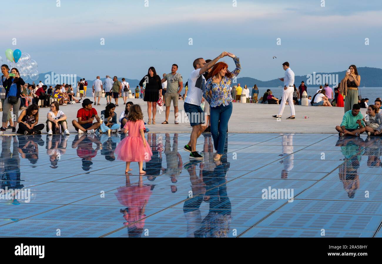 Gente che balla, altri che guardano o camminano, al sole sul Monumento al sole (noto anche come saluto al sole) a Zara, Croazia Foto Stock