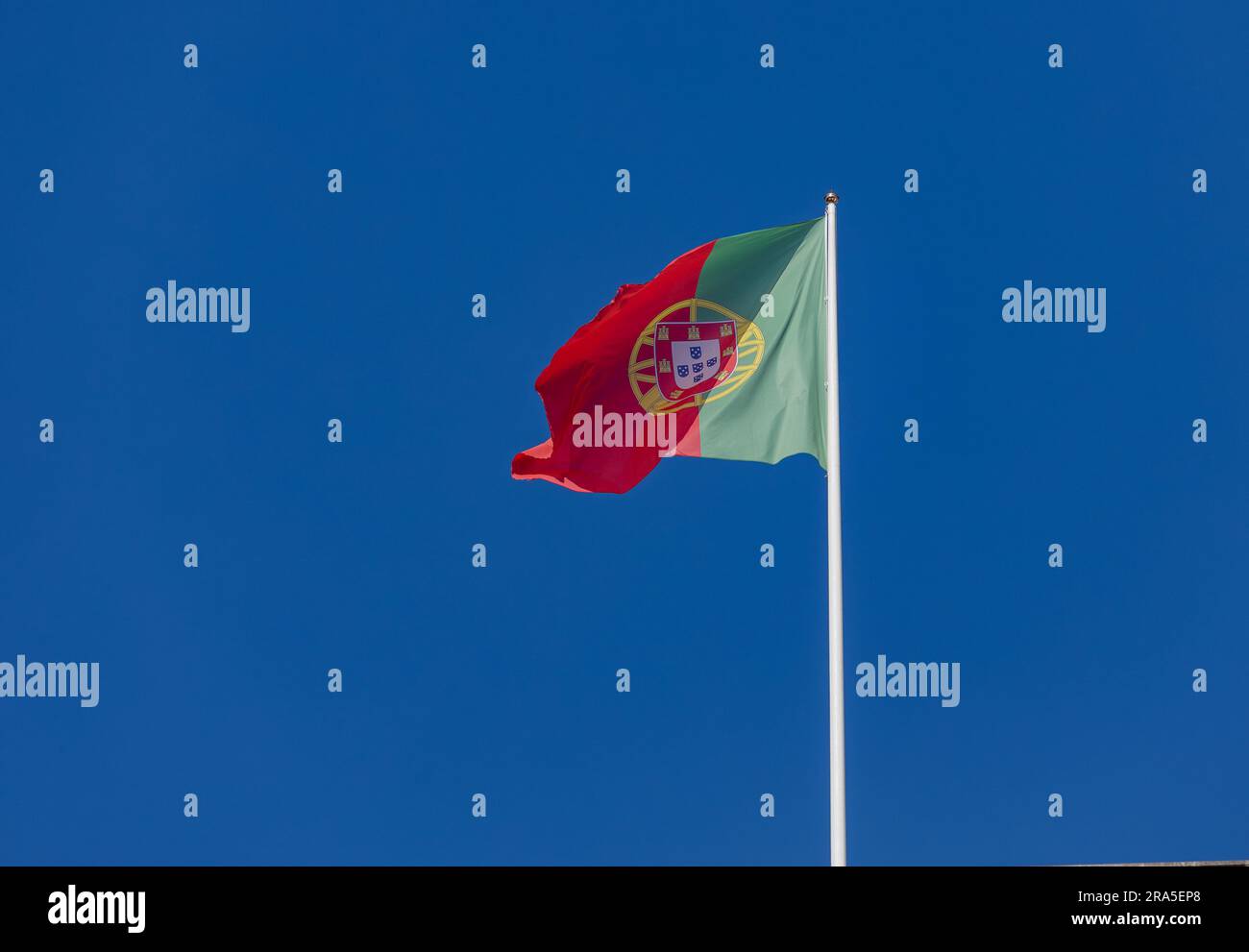 bandiera portoghese attaccata al palo che sventola sullo sfondo blu del cielo senza nuvole di vento Foto Stock